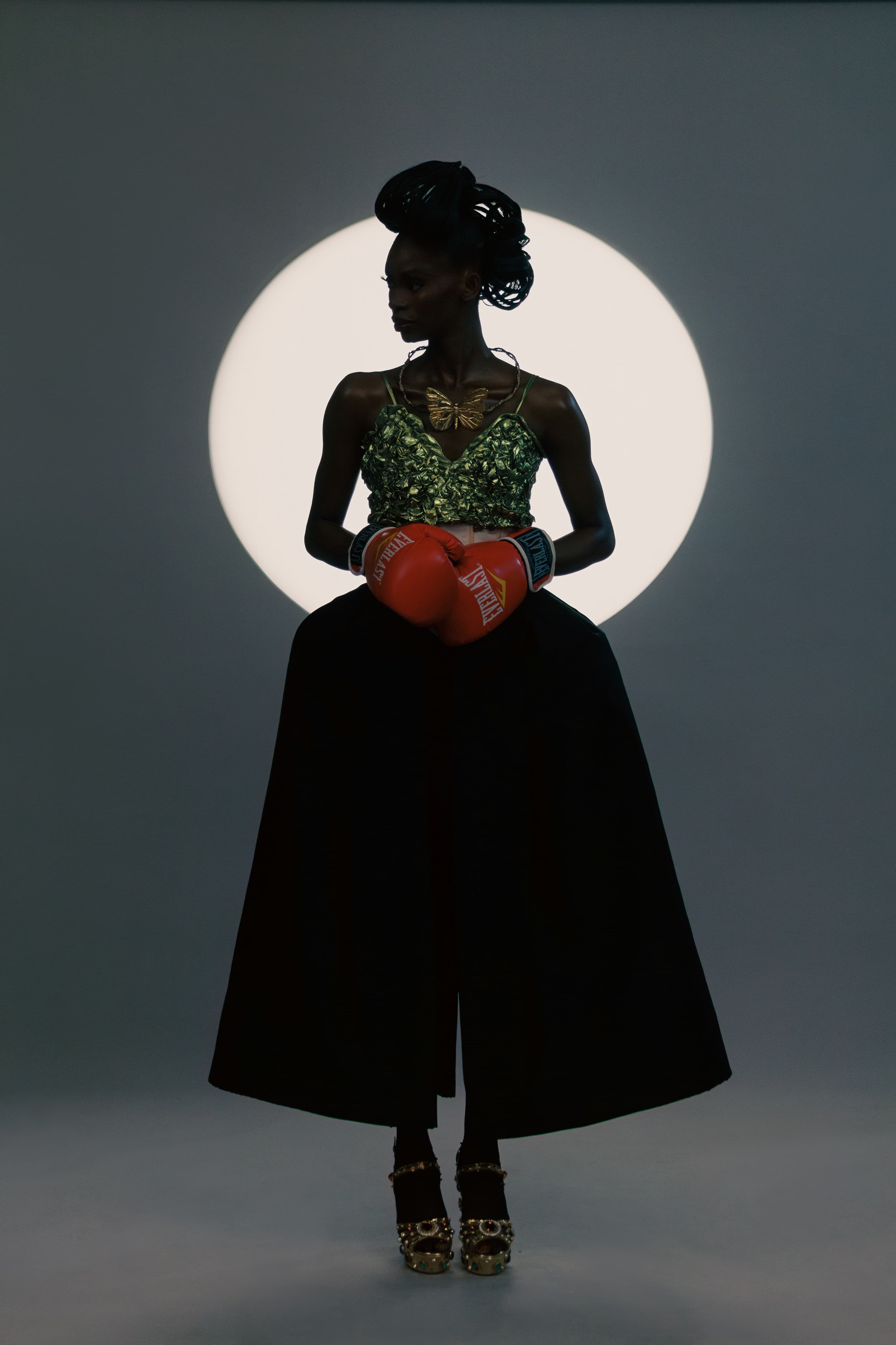 A figure in a gold-leaf corset and full black skirt, lit by a single circle of light